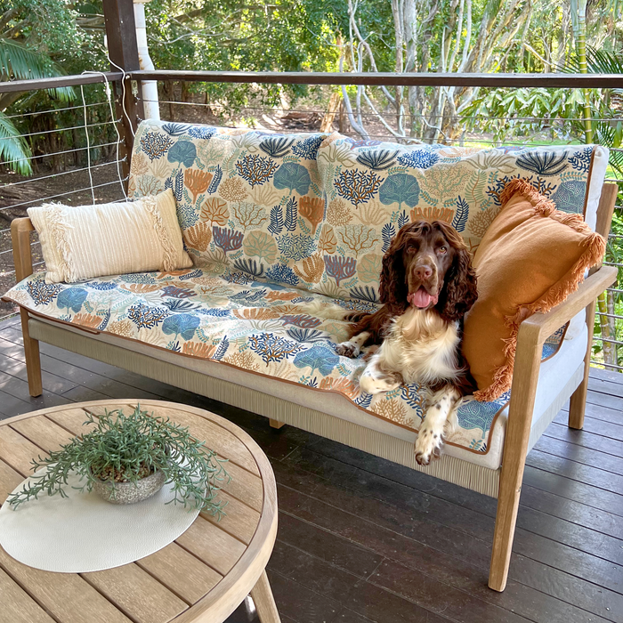 Dog sitting on Indie Boho's Coral Cove Couch Cover with a wooden table and plants in the background. Protect your couch from dog fur. Designer pet homewares an  travel accessories