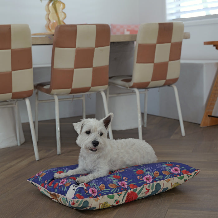 cute westie terrier lying down on a comfortable small pillow dog bed made of linen-blend material in a native flora pattern that is yellow and blue