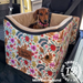 A dachshund puppy sits inside a raised fabric pet car seat with an Australian floral natives print in yellow, placed on a vehicle seat. 